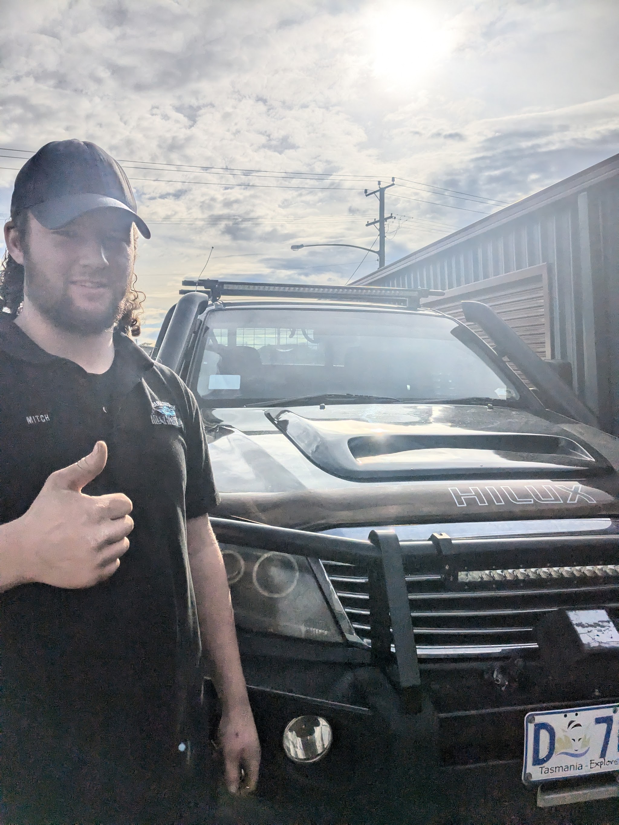 Mitch outside the workshop beside a black Hilux fitted with a bullbar, snorkel and light bar