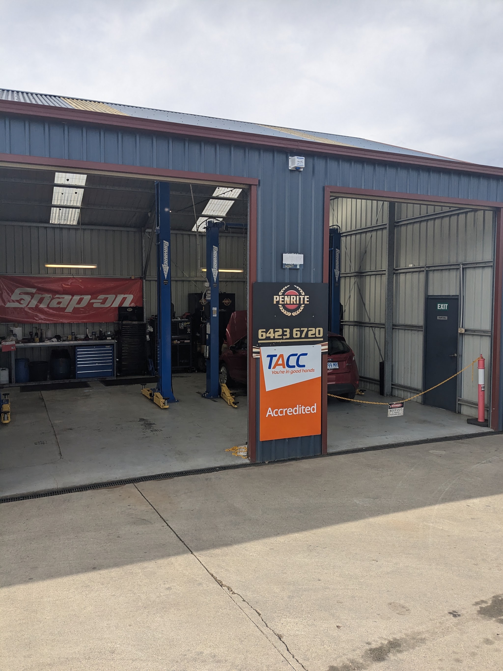 The front of the workshop, two open bays with blue hoists, a Snap-on banner and the TACC accredited sign